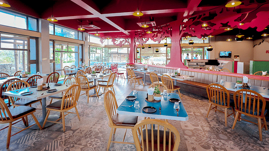 An image of a restaurant featuring chairs, tables, tree cutouts on top with ceiling lights - Pride Resort Ambaji